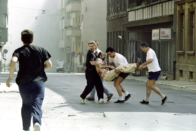 People carry a civilian who was wounded during a bombardment in the center of Sarajevo, on August 17, 1992. Seven people were reportedly killed and 44 others wounded due to heavy shelling of the city by Serbs. (Photo by Manoocher Deghati/AFP Photo)