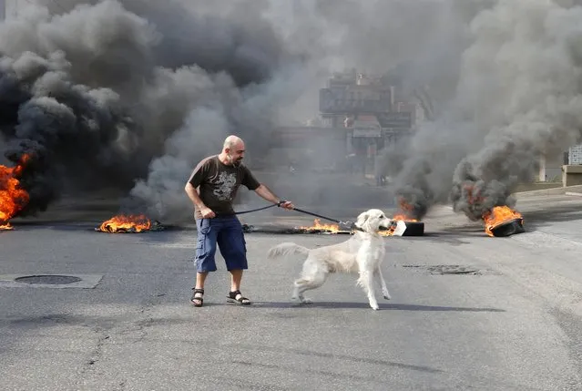 A demonstrator holds his dog as smoke rises during a protest over the deteriorating economic situation in Jdeideh, Lebanon, October 18, 2019. (Photo by Mohamed Azakir/Reuters)