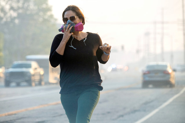 A woman covers her face as she run along Sierra Highway as the Tick Fire burns in Canyon Country, Thursday, October 24, 2019. (Photo by Hans Gutknecht/MediaNews Group/Los Angeles Daily News via Getty Images)