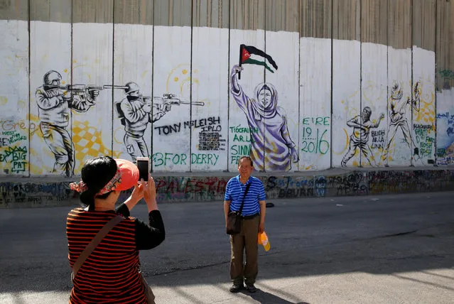 A foreigner takes a picture with her mobile phone near a graffiti painted on the controversial Israeli barrier in the West Bank town of Bethlehem, May 2, 2016. (Photo by Ammar Awad/Reuters)