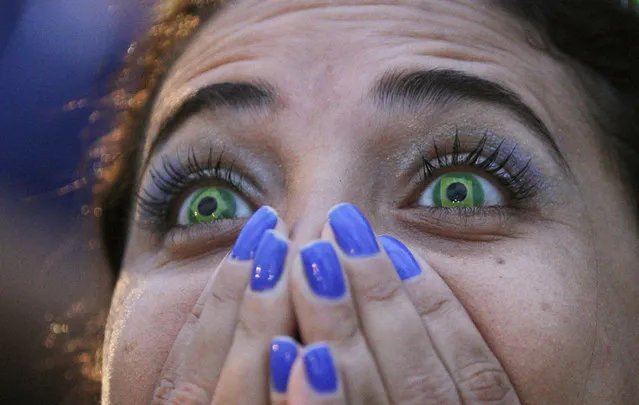 A Brazil soccer fan wearing contact lenses that mimic the Brazilian flag reacts as she watches her team play Germany in a World Cup semifinal game via live telecast inside the FIFA Fan Fest area on Copacabana beach in Rio de Janeiro, Brazil, Tuesday, July 8, 2014. (Photo by Leo Correa/AP Photo)