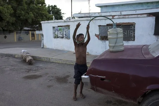 In this November 14, 2019 photo, a boy returns a hose into a jug after siphoning gas into the family car in the “Altos de Milagros Norte” neighborhood in Maracaibo, Venezuela. The downfall of Maracaibo and the lake by the same name has been especially brutal. It was once the hub of Venezuela’s thriving oil industry. Critics blame two decades of socialist rule for destroying the oil industry, that today produces a fraction of what it did at its height two decades ago. The Venezuelan government blames U.S. sanctions for many of its problems. (Photo by Rodrigo Abd/AP Photo)