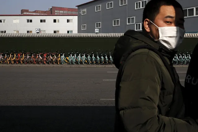 A man wearing a mask stands near a pile of bicycles from bike-sharing companies parked outside a subway station in Beijing, Monday, February 10, 2020. (Photo by Andy Wong/AP Photo)