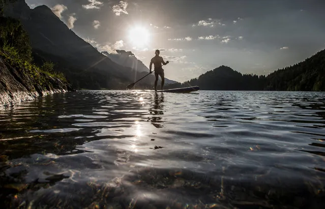 A man stands on a stand up paddle board on lake Hintersteiner in the Austrian village of Scheffau, Austria, August 2 , 2017. (Photo by Dominic Ebenbichler/Reuters)