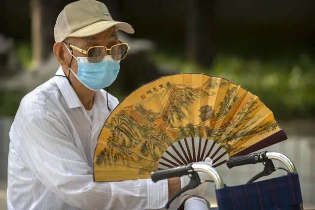An elderly man wearing a face mask fans himself at a public park in Beijing, Friday, July 8, 2022. The Chinese capital Beijing appears to have backed off a plan to launch a vaccine mandate for entry into certain public spaces after pushback from residents. (Photo by Mark Schiefelbein/AP Photo)