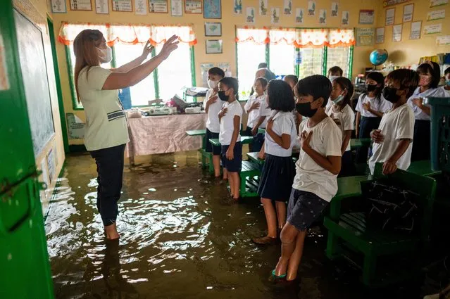 Public school teacher Mylene Ambrocio leads the singing of the Philippine national anthem during the first day of in-person classes, at a flooded school due to high tide, in Macabebe, Pampanga province, Philippines, August 22, 2022. (Photo by Lisa Marie David/Reuters)