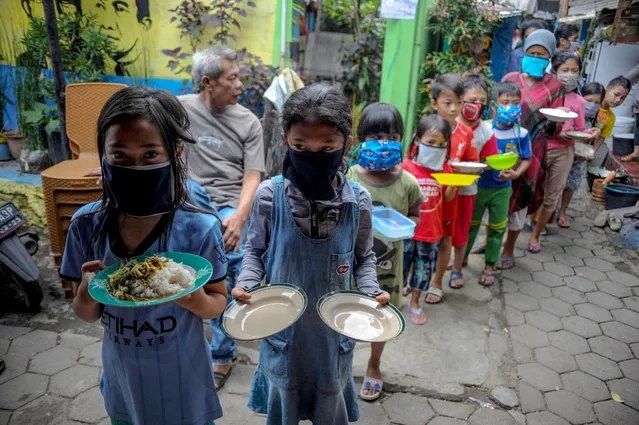 Locals wearing protective masks carry plates while queueing for food distributed for free amid the spread of coronavirus disease (COVID-19) in Bandung, West Java province, Indonesia, April 10, 2020. (Photo by Raisan Al Farisi/Antara Foto via Reuters)