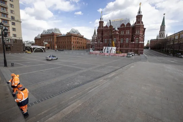 Municipal workers clean a marble wall in an empty Manege Square near Red Square in Moscow, Russia, Thursday, April 23, 2020. The authorities have ordered most city residents except those working in essential sectors to stay home through April 30 to stem the coronavirus outbreak. The new coronavirus causes mild or moderate symptoms for most people, but for some, especially older adults and people with existing health problems, it can cause more severe illness or death. (Photo by Alexander Zemlianichenko/AP Photo)