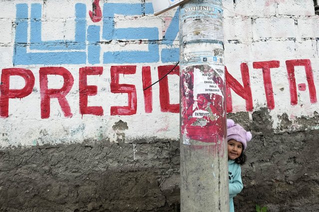A girl peeks out from behind a post in front of a campaign mural promoting presidential candidate Luisa Gonzalez, who clinched second place to compete in the April presidential run-off election, in Saquisili, Ecuador, February 11, 2025. (Photo by Dolores Ochoa/AP Photo)