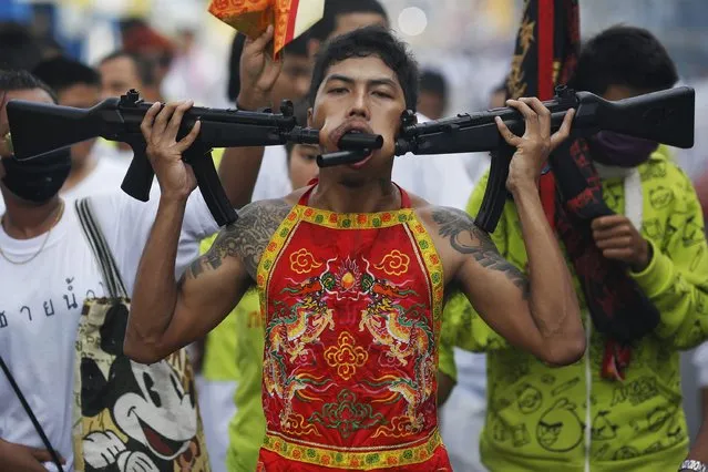 A devotee of the Chinese Bang Neow Shrine, with two plastic guns pierced through his cheeks, takes part in a street procession celebrating the annual vegetarian festival in Phuket September 29, 2014. (Photo by Damir Sagolj/Reuters)
