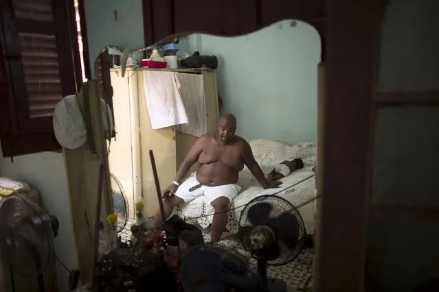 Public park caretaker Idalberto Diaz, 55, rests in a bed beside his 6-month-old granddaughter Lia, before a ceremony in a house known as Cabildo, or religious house by Santeria tradition, in downtown Havana, August 7, 2015. (Photo by Alexandre Meneghini/Reuters)