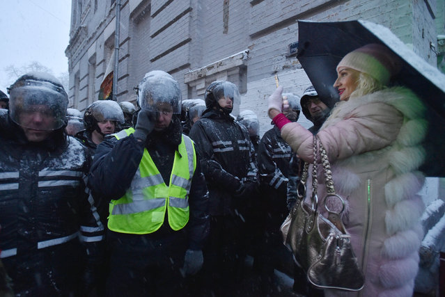 A woman takes pictures of policemen as they observe supporters attending a rally in support of arrested former Georgian President Mikheil Saakashvili outside a detention centre in Kiev on December 10, 2017. Ukrainian police re-arrested Saakashvili after a similar attempt to detain the opponent of Ukranian President Petro Poroshenko had failed. (Photo by Genya Savilov/AFP Photo)