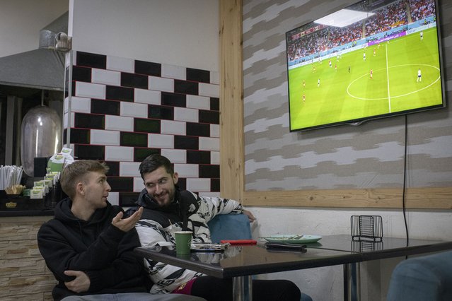 Hlib Kuian, left, and Roman Kryvyi watch a World Cup soccer match on a screen at Mazza Cafe kebab-stand, in Irpin, Kyiv region, Ukraine, Tuesday, November 29, 2022. For soccer lovers in Ukraine, Russia's invasion and the devastation it has wrought have created uncertainties about both playing the sport and watching it. For Ukrainians these days, soccer trails well behind mere survival in the order of priorities. (Photo by Andrew Kravchenko/AP Photo)