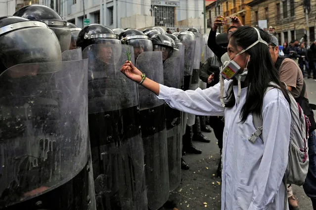 A medicine student offers a flower to a police officer in riot gear, during a protest against a new law that penalizes medical malpractice, near the Health Ministry in la Paz on January 4, 2018. .After 43 days of protests rejecting a law of the new penal code which penalizes medical malpractice, on Thursday President Morales asked Congress to revoke the controversial 205 article and doctors to suspend the strike. (Photo by Jorge Bernal/AFP Photo)