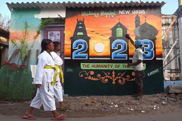 An artist (R) gives finishing touches to a New Year mural painted on his house in Chennai on December 29, 2022. (Photo by Arun Sankar/AFP Photo)