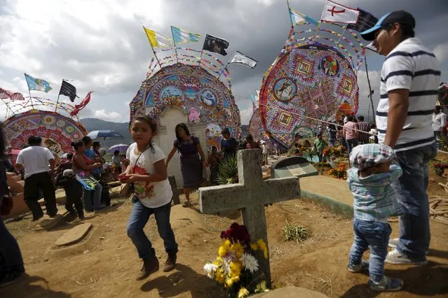 People stand in the middle of the graves and in front of giant kites in the cemetery of Santiago Sacatepequez, Guatemala, November 1, 2015. (Photo by Jorge Dan Lopez/Reuters)