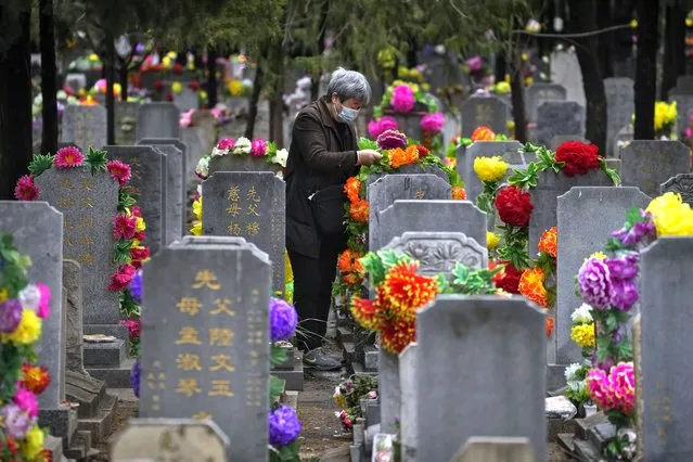 An elderly woman places flowers on a tomb during Qingming festival also known as Tomb Sweeping Day when family members visit their ancestral graves to clean up and burn offerings in Beijing, Wednesday, April 5, 2023. (Photo by Andy Wong/AP Photo)