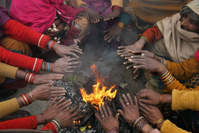 In this December 22, 2014 photo, Indian passengers warm themselves around a fire as they wait for their train to arrive on a cold morning, in Allahabad, India, Monday. Cold wave conditions intensified across northern India as temperatures dipped along with thick blankets of fog cutting out sunlight. (Photo by Rajesh Kumar Singh/AP Photo)
