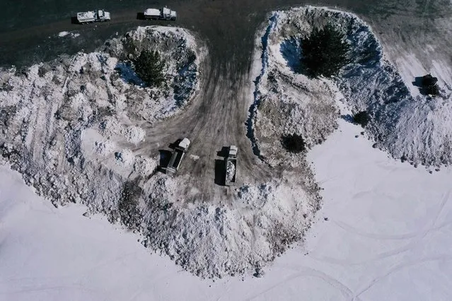 An aerial image shows trucks unloading snow removed from roads to a permitted area on the edge of town where it can melt safely rather than blocking drains and causing flooding as it melts following record snow fall from winter storms in Mammoth Lakes, California on April 6, 2023. (Photo by Patrick T. Fallon/AFP Photo)