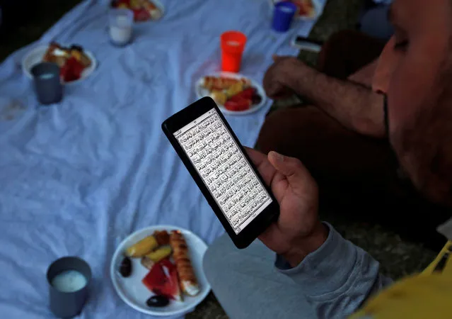 A Muslim man reads the Koran on his mobile as he waits for iftar (breaking fast) outside a mosque during the holy month of Ramadan in Srinagar June 4, 2018. (Photo by Danish Ismail/Reuters)
