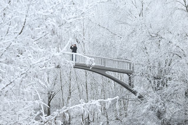 A man takes a picture as he crosses a bridge after snowfall in a park on the Main river embankment in Frankfurt am Main, western Germany, on December 29, 2024. (Photo by Kirill Kudryavtsev/AFP Photo)