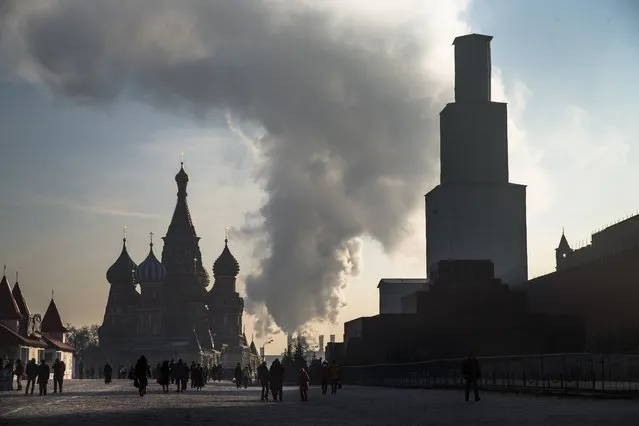 Steam rises from a power plant behind the Moskva River as tourists walk along the Red Square with St. Basil's Cathedral, at left, in Moscow, Russia, Thursday, January 22, 2014. The structure at right is the Spassky Tower, which is currently being renovated. (Photo by Alexander Zemlianichenko/AP Photo)