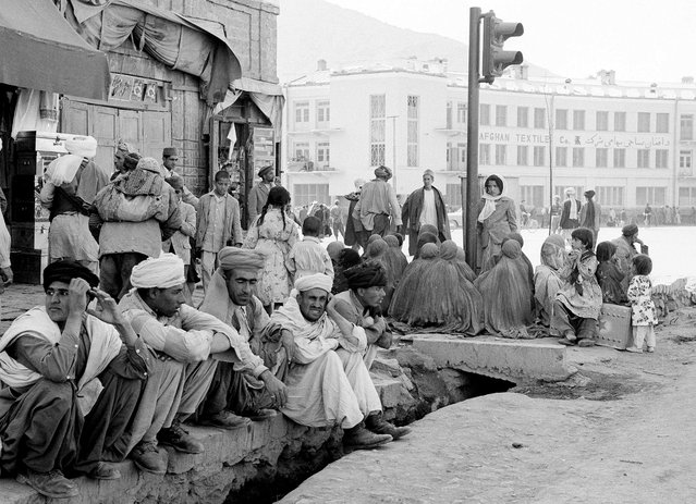 A modern traffic light stands incongruously amid burqa-clad women sitting on a Kabul street corner with their backs to their men on May 25, 1964. (Photo by Henry Burroughs/AP Photo via The Atlantic)