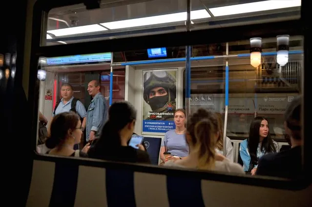 Commuters ride on a metro train next to a poster promoting contract army service and reading “Join your people!” in Moscow on June 26, 2023. (Photo by Natalia Kolesnikova/AFP Photo)