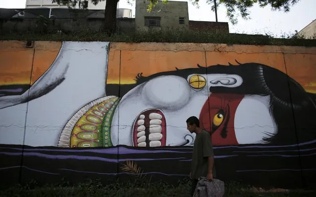 A man holds a blanket as he walks past graffiti by Brazilian artist Cranio depicting an indigenous man swimming in petroleum, on a mural highlighting the issue of severe water shortages in Sao Paulo, February 3, 2015. Residents of Brazil's largest city, Sao Paulo, could soon only have running water two days a week. (Photo by Nacho Doce/Reuters)