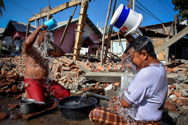 Two men bathe near their homes damaged or destroyed by an earthquake in Kayangan District, Lombok, Indonesia August 11, 2018  in this photo taken by Antara Foto. (Photo by Ahmad Subaidi/Antara Foto via Reuters)