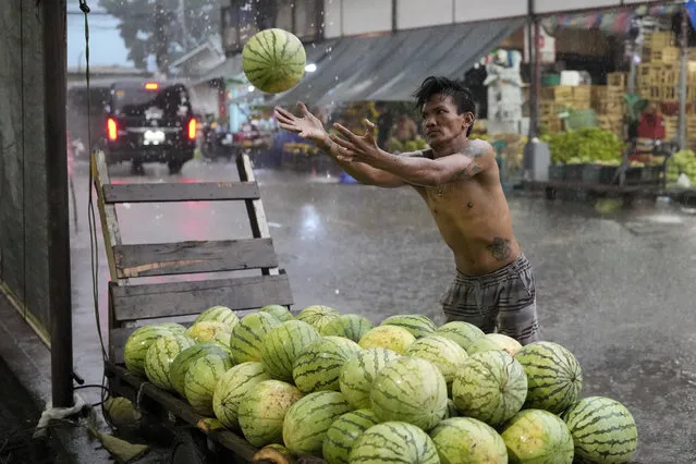 A worker catches watermelons during a downpour at a fruit market in Quezon City, Philippines, Thursday, July 13, 2023. (Photo by Aaron Favila/AP Photo)