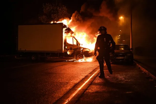 A French anti riot police officer walk past a burning truck in Nantes, western France on early July 1, 2023, four days after a 17-year-old man was killed by police in Nanterre, a western suburb of Paris. French President Emmanuel Macron has announced measures including more police and urged parents to keep minors off the streets as he battled to contain nightly riots over a teenager's fatal shooting by an officer in a traffic stop. (Photo by Sebastien Salom-Gomis/AFP Photo)