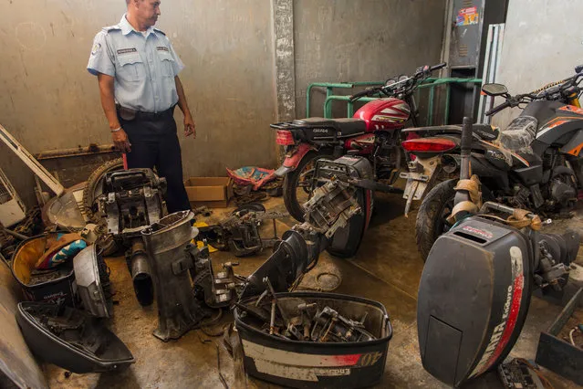 In this November 11, 2016 photo, a municipal police officer stands amid stolen engines seized from pirates, at the police station in Punta de Araya, Sucre state, Venezuela. “People can't make a living fishing anymore, so they're using their boats for the options that are left: smuggling gas, running drugs, and piracy”, said Jose Antonio Garcia, leader of the state's largest union. (Photo by Rodrigo Abd/AP Photo)