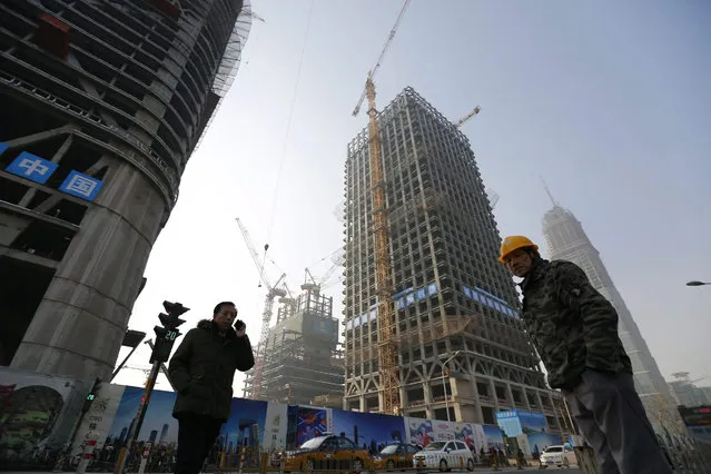 A migrant worker and a Chinese man walk passing by a construction site in central business district (CBD) of Beijing, China, 19 January 2016. China's economy grew 6.9 percent in 2015, according to official figures released 19 January, marking the slowest growth in more than a quarter of a century. The growth missed the 7-per-cent target that the government had set for the year and is the weakest since 1990. It matched predictions of 6.9 percent by economists. (Photo by Wu Hong/EPA)