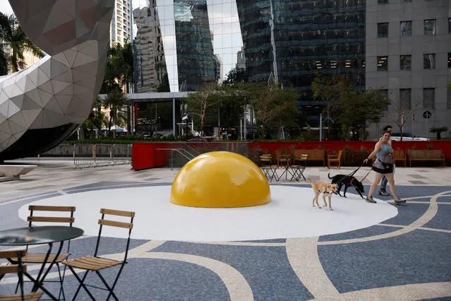 People with dogs walk past the “Art Eggcident” installation by Dutch artist Henk Hofstra at Faria Lima Avenue, in Sao Paulo, Brazil on September 18, 2023. (Photo by Amanda Perobelli/Reuters)