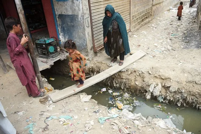 In this photo taken on September 21, 2023, an Afghan girl and her mother cross a sewer line at an Afghan refugee camp in Karachi. (Photo by Rizwan Tabassum/AFP Photo)
