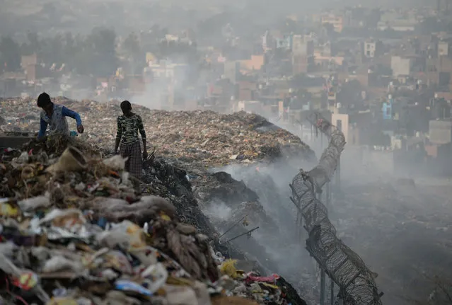 Indian ragpickers collect usable material as smoke rises from a garbage dump at the Bhalswa landfill site in New Delhi, on October 29, 2018. Pollutants from vehicles, burning garbage dumps, building sites and farmers burning crops in regions outside the Indian capital spike in levels during winter in Delhi when air quality often eclipses the World Health Organization's safe levels. (Photo by Sajjad Hussain/AFP Photo)