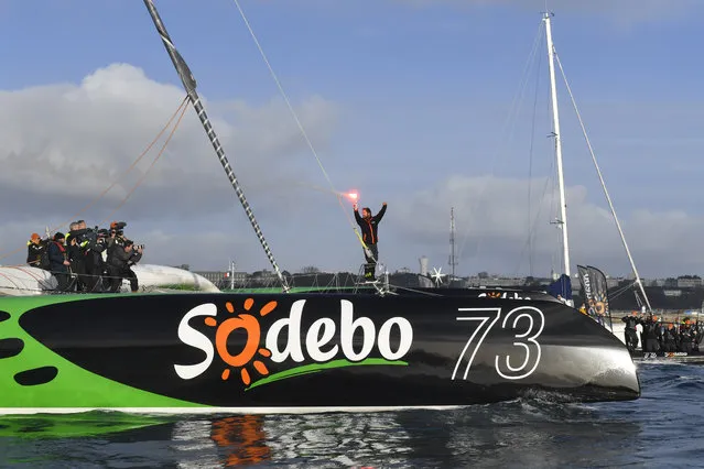 French skipper Thomas Coville (C) holds a burning flare onboard his “Sodebo Ultim” multihull as he arrives in the port of Brest, western France, on December 26, 2016, after beating the record in solo non-stop round the world sailing. Coville, 48, slashed eight days off the record when he ended an astonishing solo non-stop circumnavigation of the World on his 31m maxi trimaran on December 25, 2016, in just 49 days, 3 hours, 7mins and 38secs. (Photo by Damien Meyer/AFP Photo)