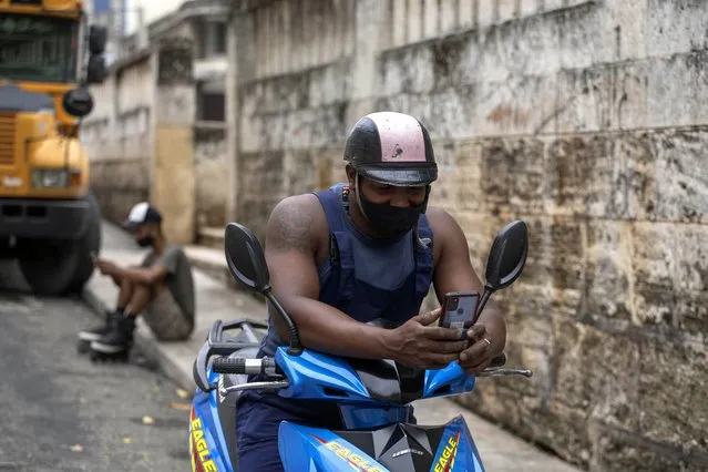 Men use a pre-paid public wifi connection on their cell phones next to a park that's popular for connectivity, which costs money, in Havana, Cuba, Tuesday, July 14, 2021. (Photo by Eliana Aponte/AP Photo)