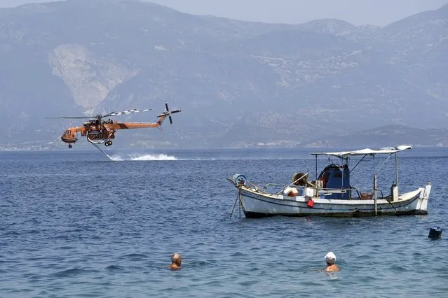 A helicopter fills up with water from the sea near Ziria village, east of Patras, Greece, Sunday, August 1, 2021. A wildfire that broke out Saturday in western Greece forced the evacuation of four villages and people on a beach by the Fire Service, the Coast Guard and private boats, authorities said. (Photo by Andreas Alexopoulos/AP Photo)