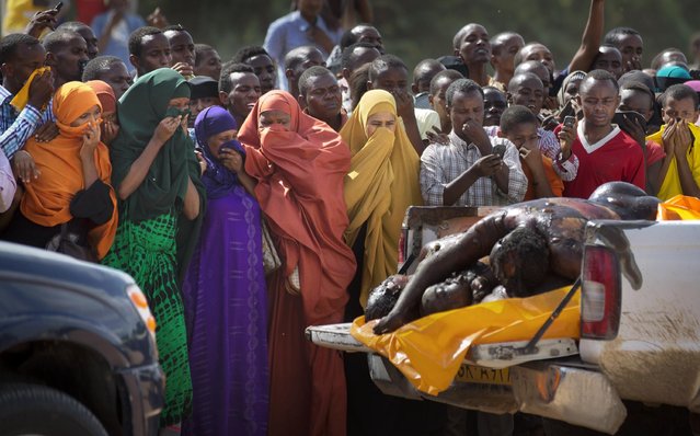 Women in the crowd cover their faces to protect against the smell as authorities display the bodies of the alleged attackers before about 2,000 people in a large open area in central Garissa, Kenya Saturday, April 4, 2015. Authorities displayed the bodies of the alleged attackers involved in the killings at Garissa University College on the bed of a pickup truck that drove slowly past the crowd, which broke into a run in pursuit. (Photo by Ben Curtis/AP Photo)