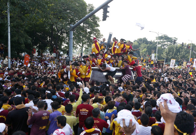 Filipino Roman Catholic devotees climb the carriage to kiss and rub with their towels the image of the Black Nazarene to celebrate its feast day Monday, January 9, 2017 in Manila, Philippines. (Photo by Bullit Marquez/AP Photo)