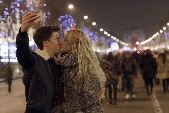 A man takes a picture as he kisses his companion during the New Year's Eve celebration on the Champs Elysees, in Paris, France, Sunday, January1, 2017. (Photo by Christophe Ena/AP Photo)