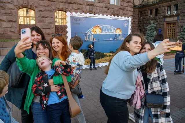 People take selfies in front of an artwork depicting Kerch bridge on fire, amid Russia's attack on Ukraine, in central Kyiv, Ukraine on October 8, 2022. (Photo by Vladyslav Musiienko/Reuters)