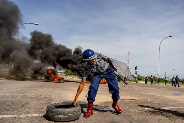 A police officer removes tyres set by protesters during a “stay-away” demonstration against the doubling of fuel prices on January 14, 2019 in Emakhandeni township, Bulawayo. Zimbabwe's President on January 12 announced a more than 100 percent rise in the price of petrol and diesel in a move to improve supplies as the country struggles with its worst fuel shortages in a decade. In the city of Bulawayo, demonstrators attacked minibuses heading to the city centre and used burning tyres and stones to block the main routes into town. (Photo by Zinyange Auntony/AFP Photo)