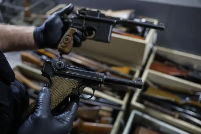 A German Luger P08 from World War II is held by a gunsmith in front of boxes of weapons is seen in a box of weapons in Strasbourg, eastern France, Wednesday, November 30, 2022. France has launched a nationwide drive to collect millions of old firearms, remnants of the two World Wars or long-abandoned hunting excursions. French Interior Ministry officials suspect French families keep many unregistered weapons tucked away in attics and storerooms as heirlooms in the country that was once the scene of many of the last century's fiercest battles. (Photo by Jean-Francois Badias/AP Photo)