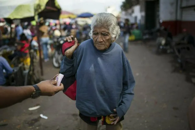 An elderly woman is offered cash as she begs at a wholesale food market in Caracas, Venezuela, Monday, January 28, 2019. (Photo by Rodrigo Abd/AP Photo)