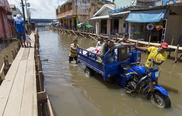 Residents push a motorcycle in the town of Tabatinga inundated with floodwaters from the Solimoes River in the state of Amazonas April 26, 2015. According to the state Civil Defense, more than 20,000 families were affected in the State with strong rains. The region is in the Triple Border between Brazil, Colombia and Peru. (Photo by Bruno Kelly/Reuters)