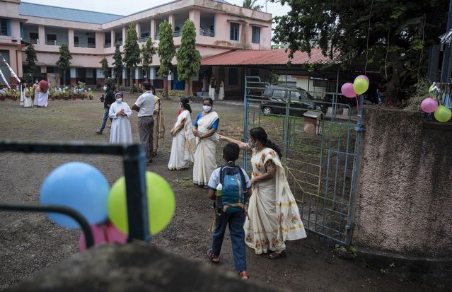 A teacher guides a student to his classroom as schools reopened in Kochi, Kerala state, India, Monday, November 1, 2021. Schools in this southern state that had remained closed for nearly twenty months due to the coronavirus pandemic reopened Monday. (Photo by R.S. Iyer/AP Photo)