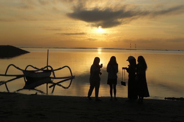 People watch the sun rise on Sanur Beach in Denpasar, Bali, Indonesia, Thursday, October 28, 2021. Indonesians are looking ahead warily toward the upcoming holiday travel season, anxious for critical tourist spending but at the same time worried that an influx of millions of visitors could lead to a new coronavirus wave just as the pandemic seems to be getting better. (Photo by Firdia Lisnawati/AP Photo)